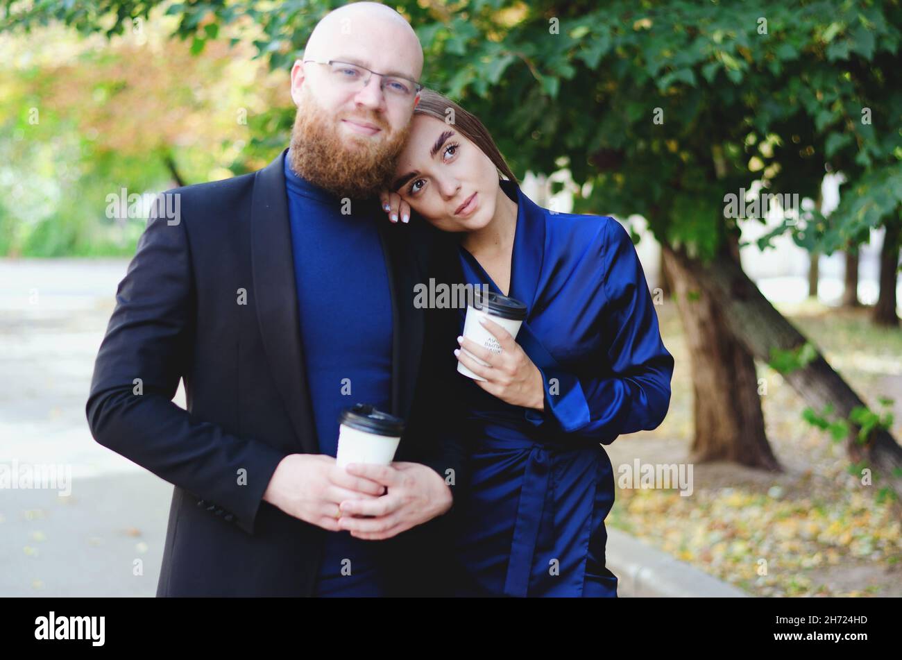 Happy family, couple drinking coffee in city. Urban love story of a stylish young business man in a blue suit with a red beard. And attractive woman Stock Photo