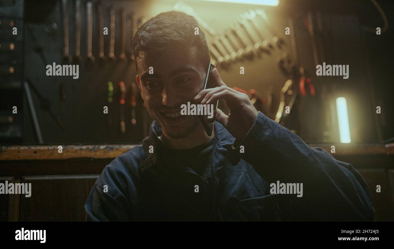 Handsome determined blacksmith man sitting in front of the workbench and he using smartphone call friends or her family Stock Photo