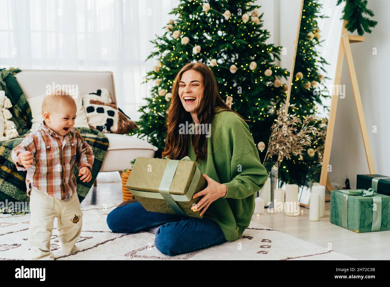 Happy cheerful laughing young mother with toddler near the Christmas tree receive Christmas gifts. Stock Photo