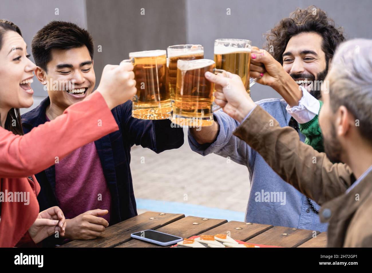 Multiracial friends having fun chearing with beers at brewery bar restaurant outdoor - Focus on Stock Photo