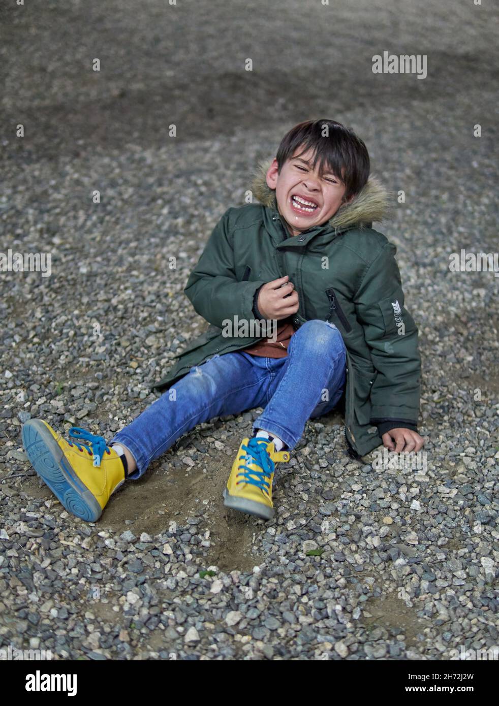 brunette child sitting on the ground crying inconsolably with closed eyes in wintertime outdoors with a parka. vertical. concept of frustration in chi Stock Photo