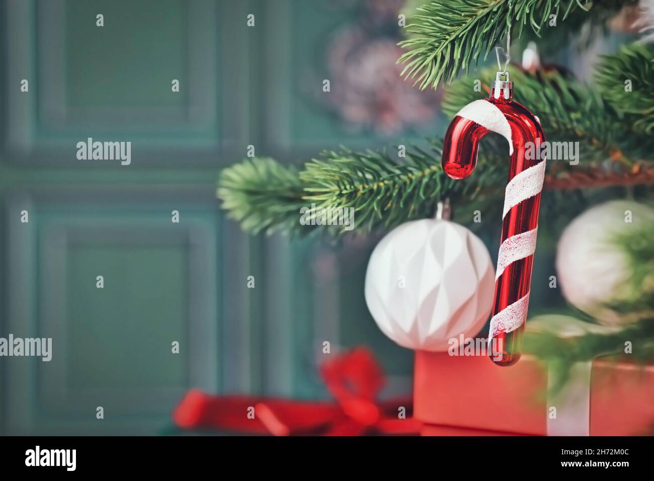 Candy cane christmas ornament on tree with gifts on side of green ...