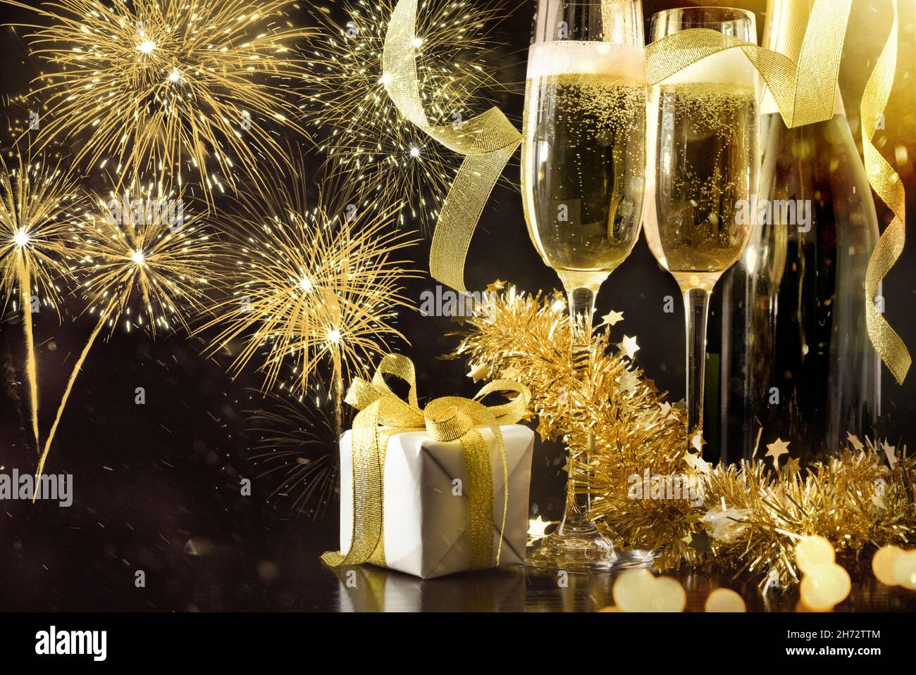 New year's eve party celebration background with sparkling wine glasses and bottle decorated with gift ribbons and golden decoration on black table an Stock Photo