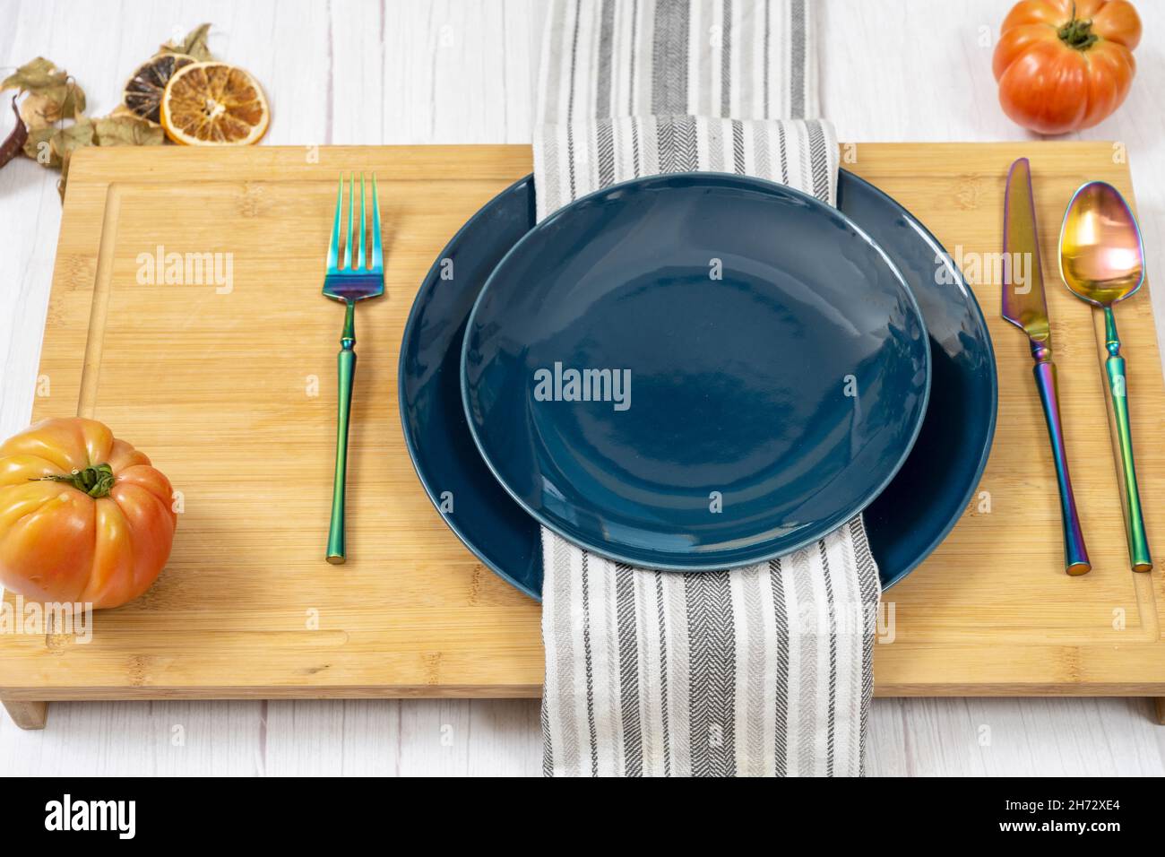 Dinner set with blue plates, iridescent cutlery and pink tomatoes on bamboo table Stock Photo