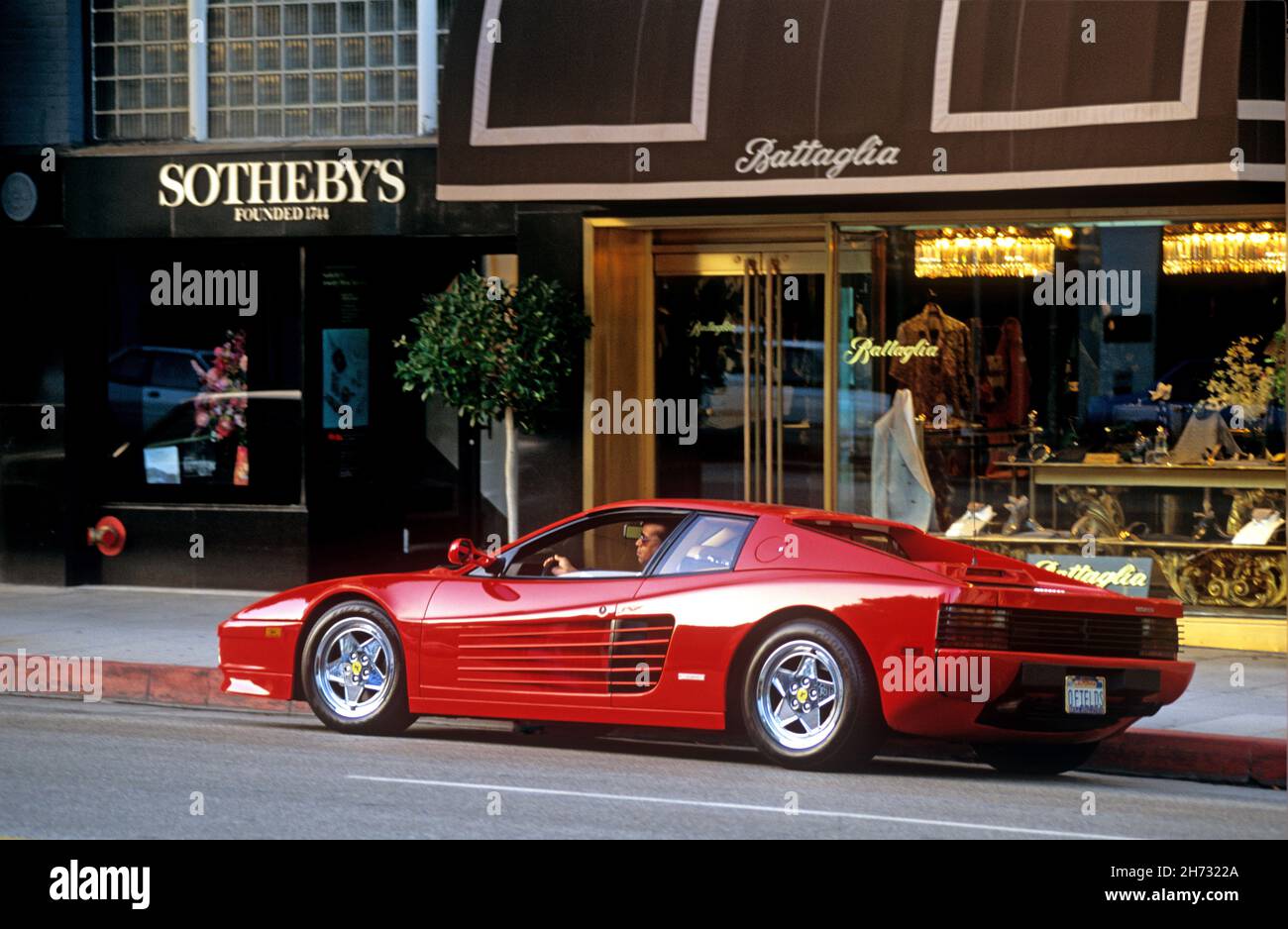 Man sitting in a red Ferrari sports car parked on Rodeo Drive in Beverly Hills, CA Stock Photo