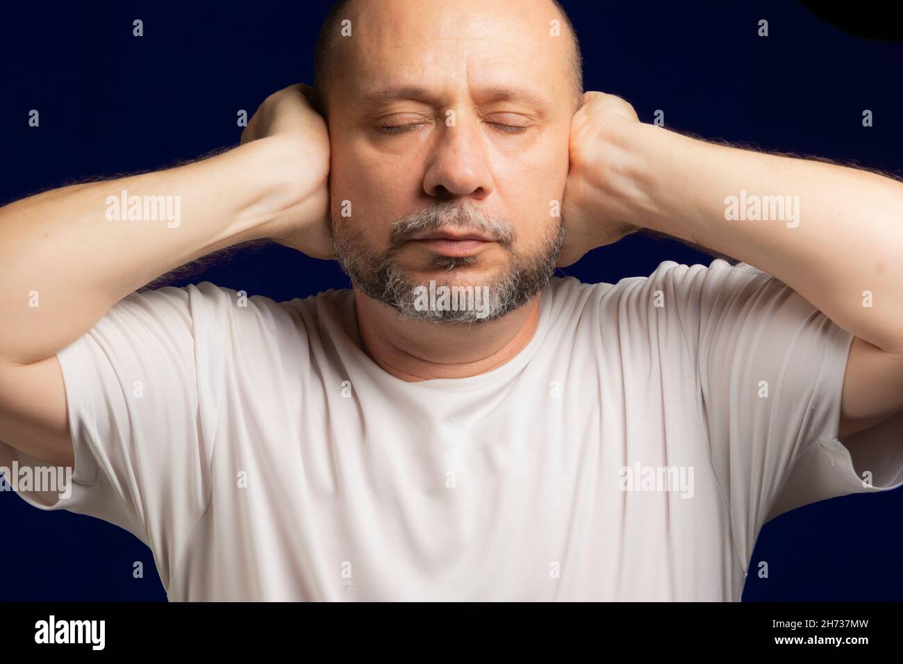 Person with hands on ears against dark blue background. Salvador, Bahia, Brazil. Stock Photo