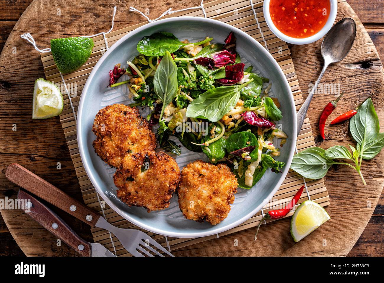 Delicious Thai fish cakes with asian salad and sweet chili sauce on a rustic wood table top. Stock Photo