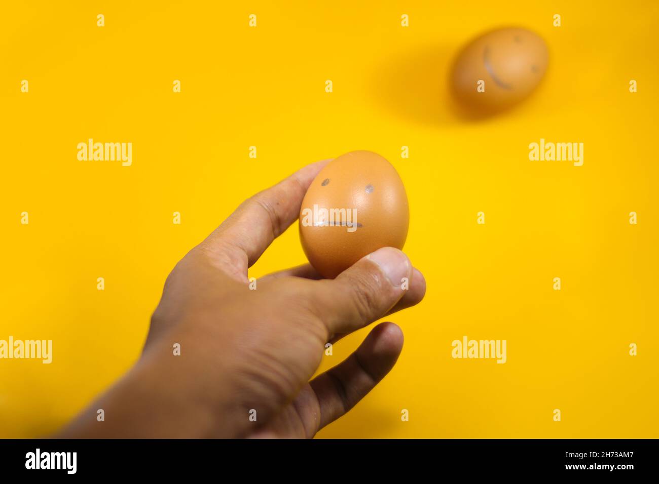 Hand choosing sad face brown egg on orange background. Conceptual Illustration for questionnaire, feedback rating, customer review, experience Stock Photo