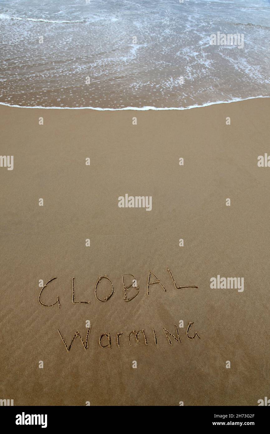 Global warming written in the sand at beach with rising wave Stock Photo