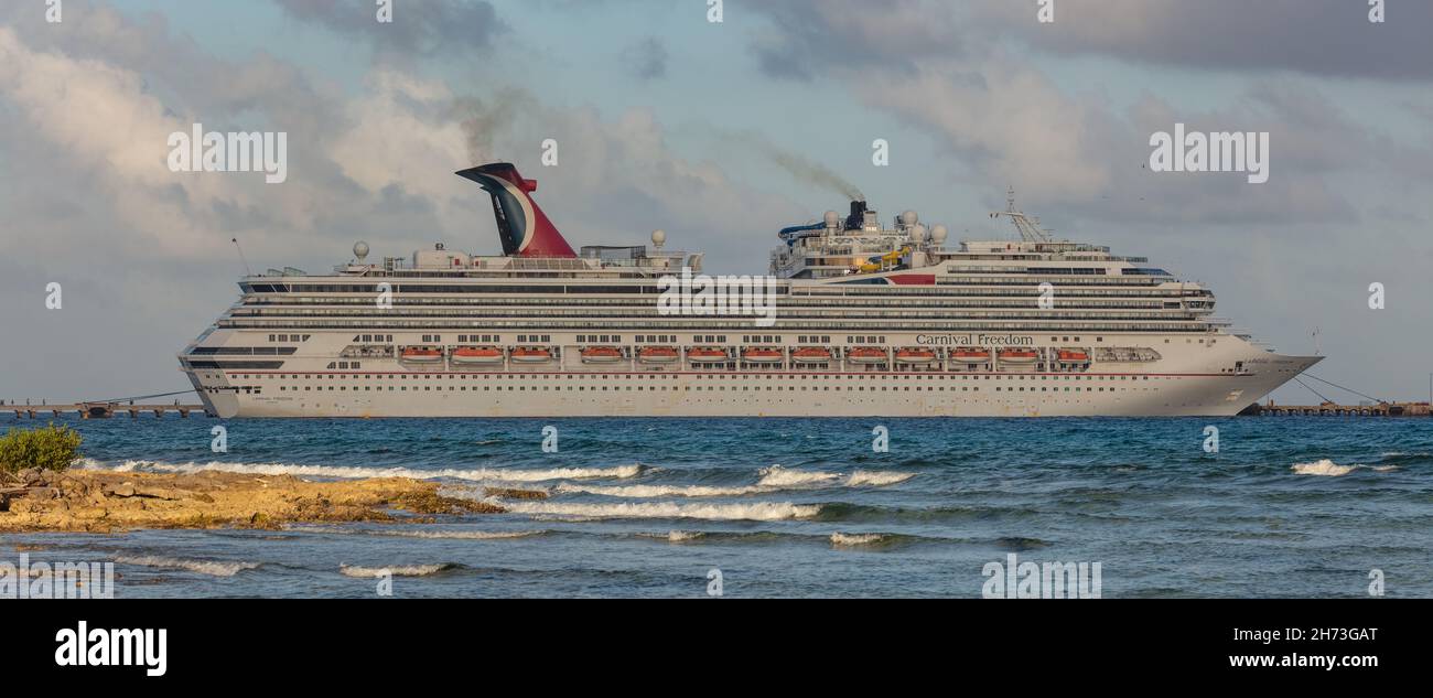 Cozumel, Mexico - February 11, 2020: Beautiful panoramic shot of Carnival Freedom docked in Costa Maya port. Shore line, splashing waves in the foregr Stock Photo