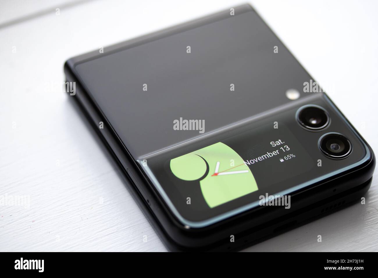 The front display of the innovative Samsung Galaxy Z Flip 3 folding phone is seen while sitting on a desk. Stock Photo