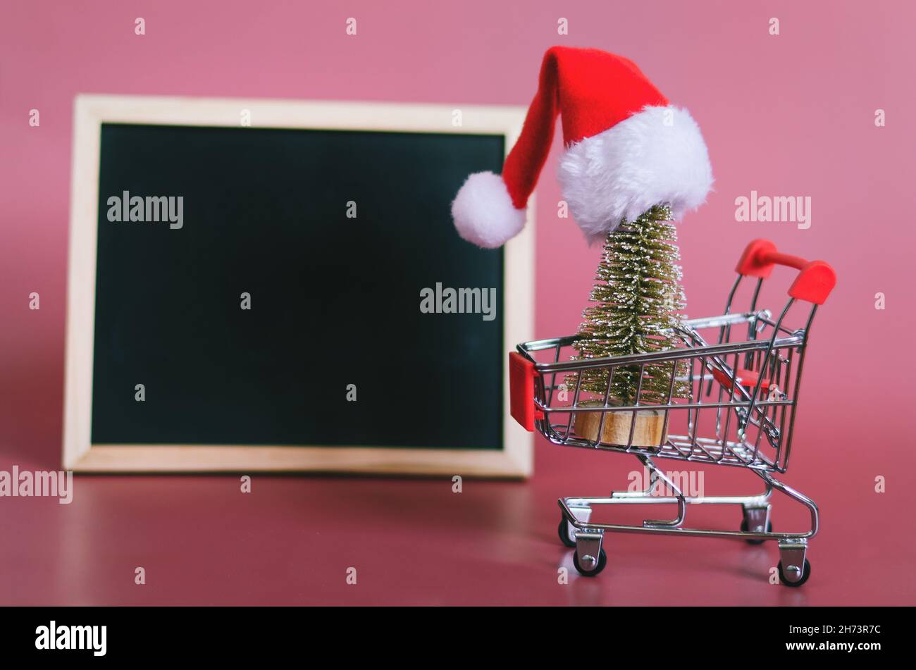 Christmas flat lay on red background with place for text. Christmas hat, toy tree, shopping trolley and a writing board. Resolutions, shopping, plan Stock Photo