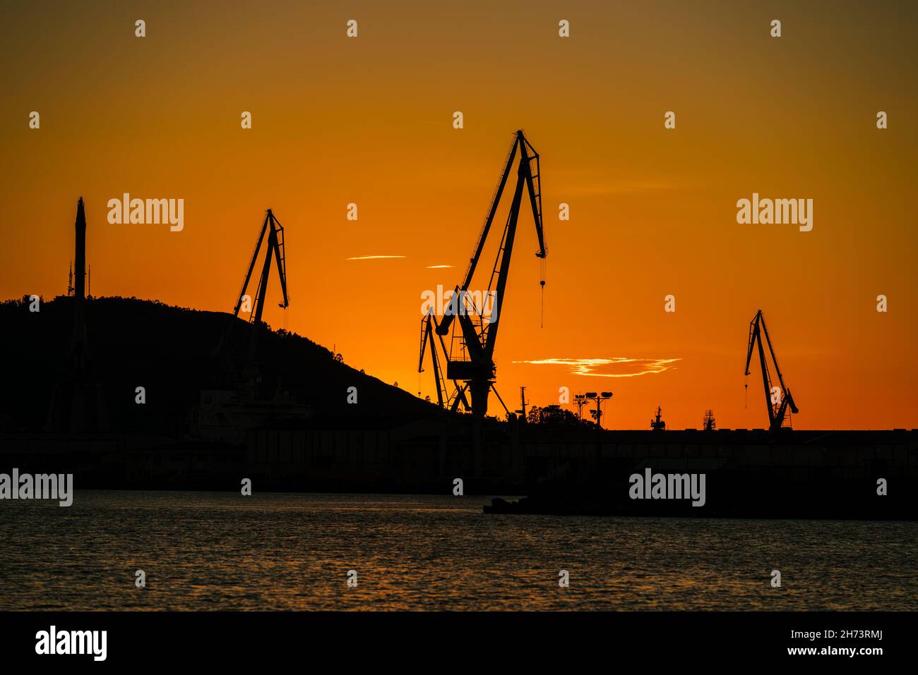 Port shipyard cranes against orange sky Stock Photo