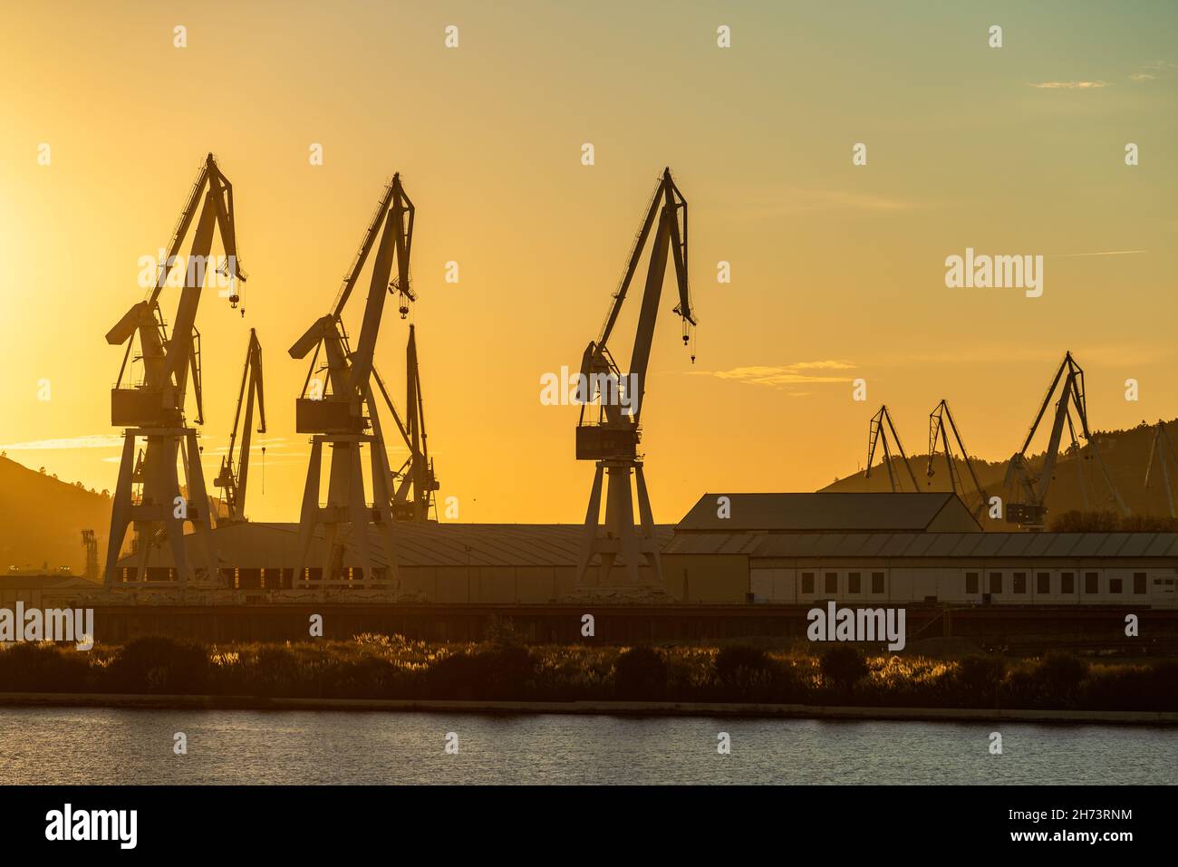 Port shipyard cranes against orange sky Stock Photo