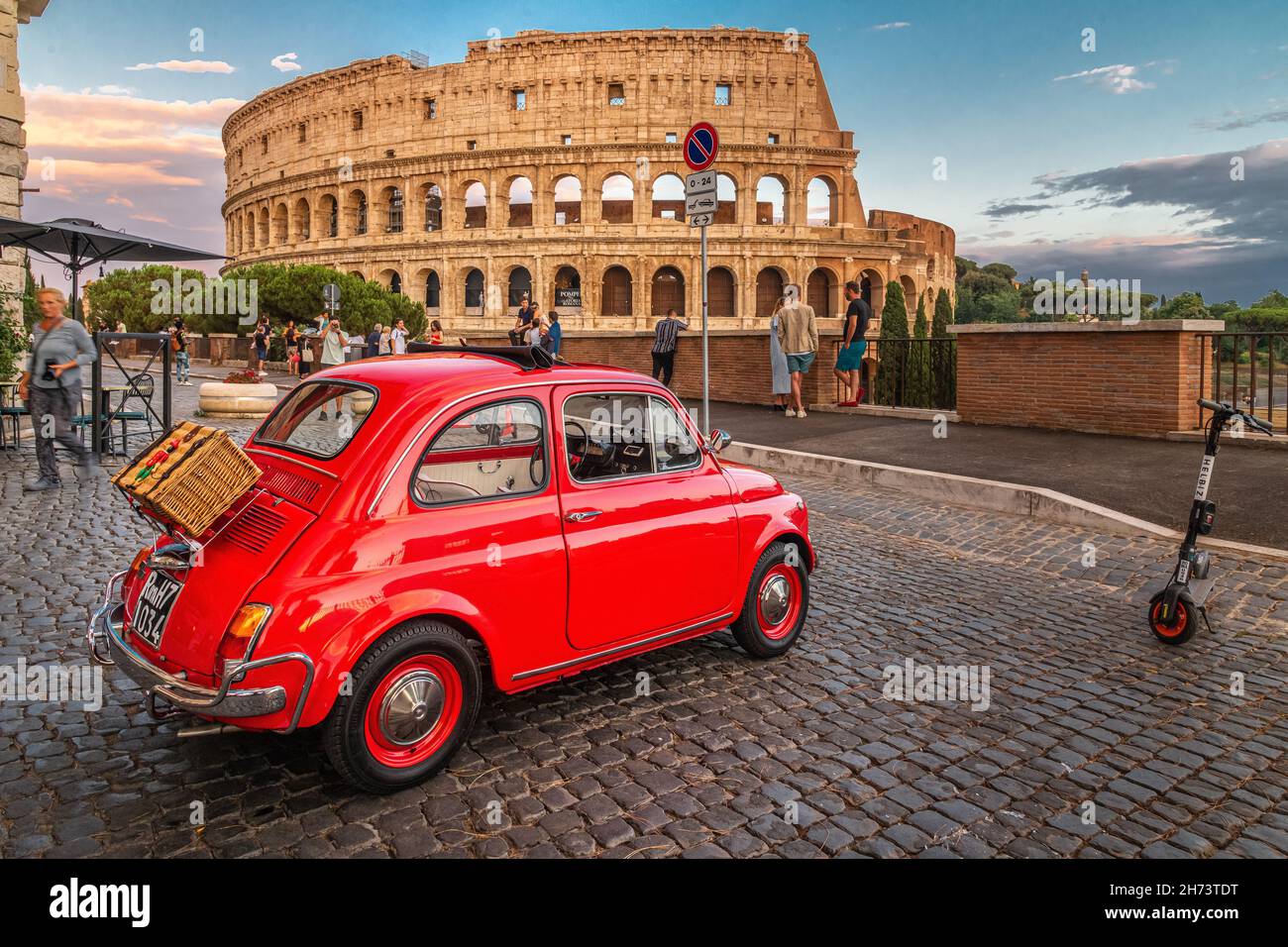 Little red old Fiat 500 near coliseum at sunset with picnic basket on