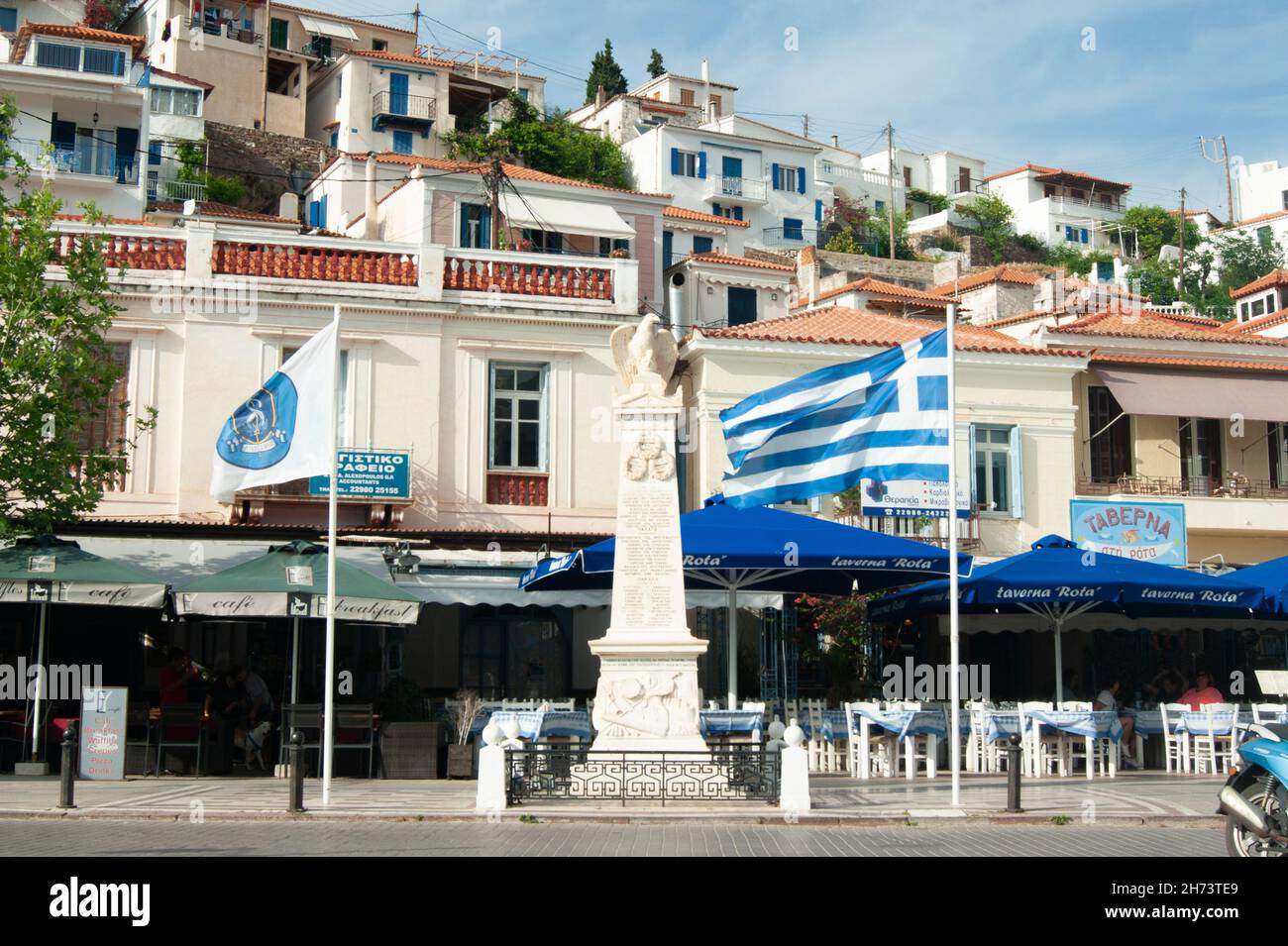 Poros town -  Greece - May 21 2018 : Busy waterfront at the charming old town. View of war memorial, with background of taverna's and bars. Landscape Stock Photo