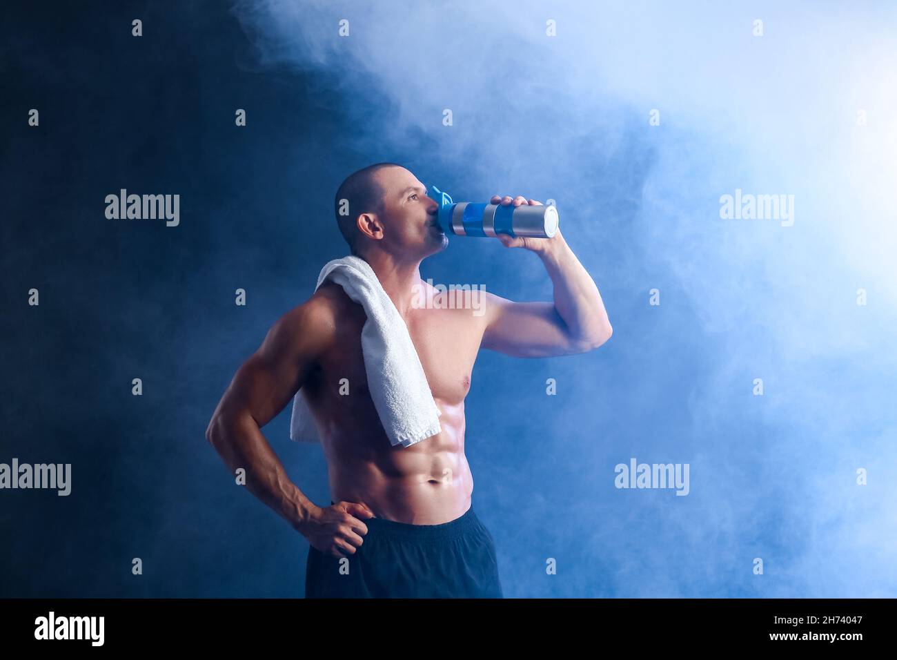 Male bodybuilder drinking protein shake in smoke on dark background