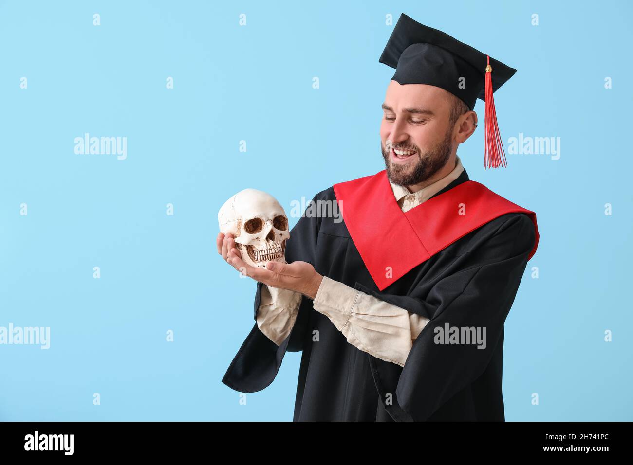 Handsome male graduate with human skull on blue background Stock Photo ...