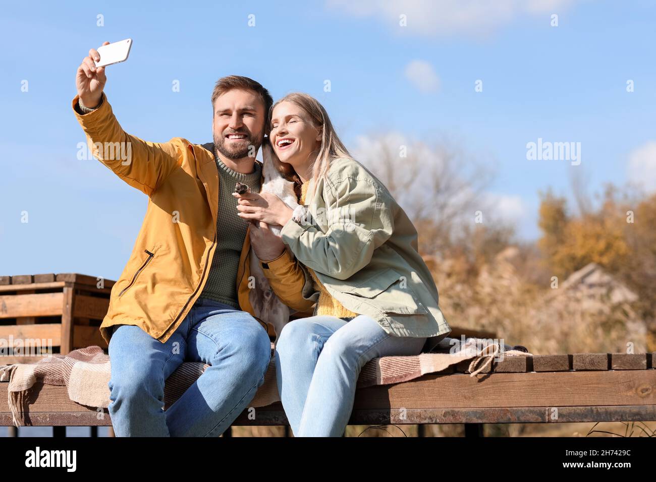 Lovely couple with cute dog taking selfie on autumn day Stock Photo