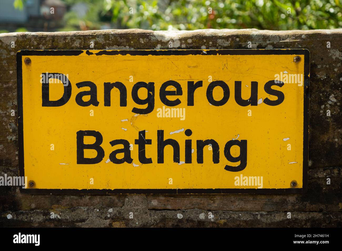 A yellow dangerous bathing warning sign fixed to a stone wall beside