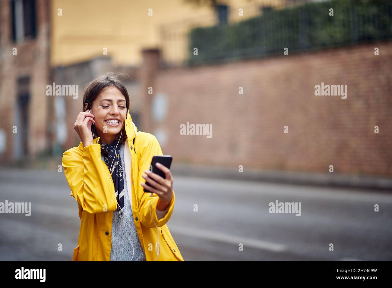 A young girl with yellow raincoat enjoying the music and a walk in a peaceful atmosphere on a cloudy day. Walk, rain, city Stock Photo