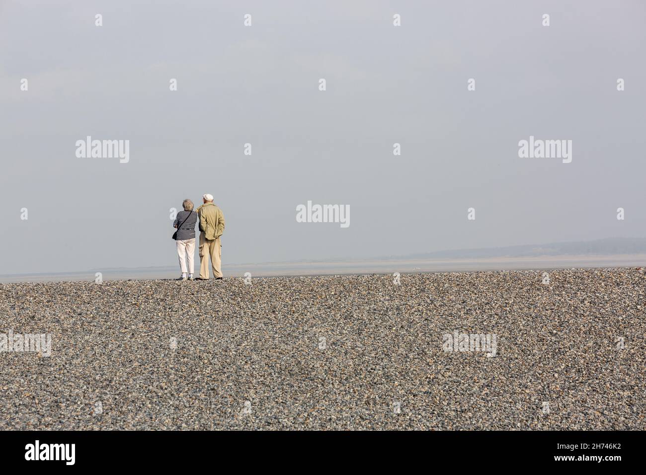 Couple on the edge of a pebble beach observing the sea. Plage du Hourdel, Baie de Somme, France Stock Photo