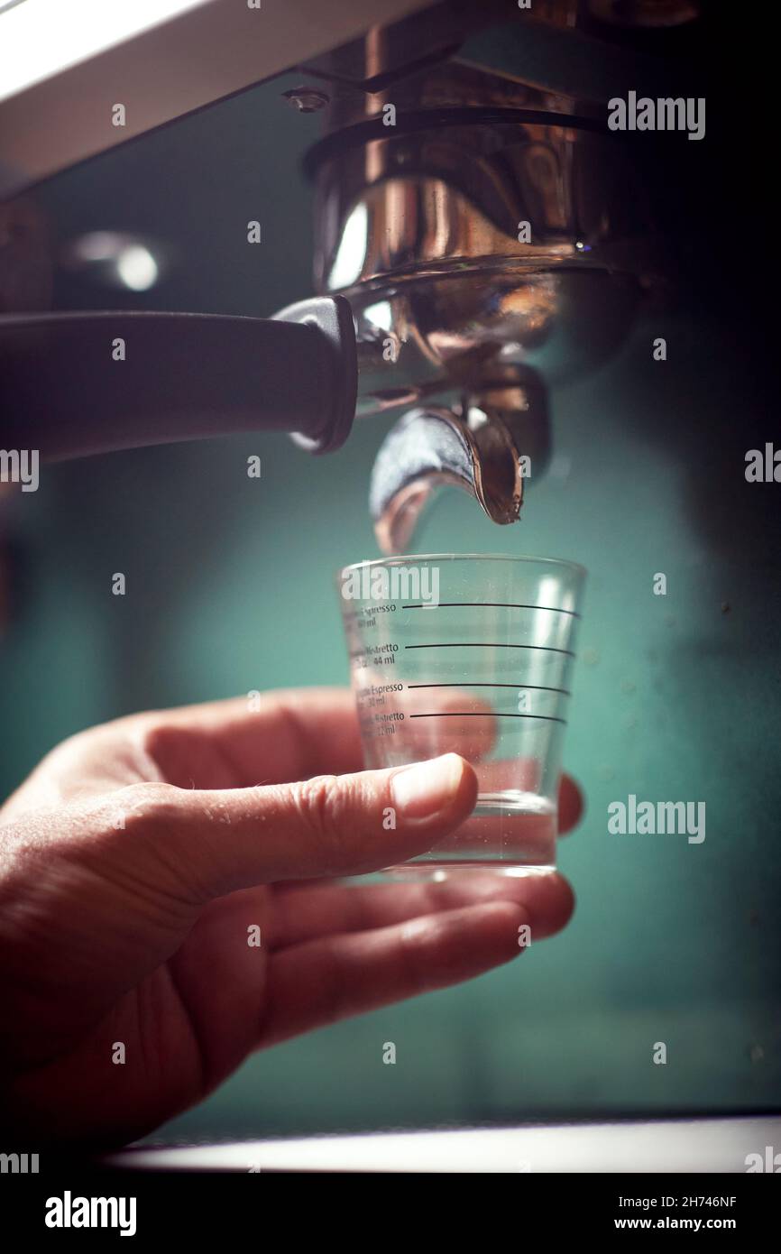 A barman holding a glass waiting for a fragrant and aromatic beverage to pour from an espresso apparatus. Coffee, beverage, bar Stock Photo