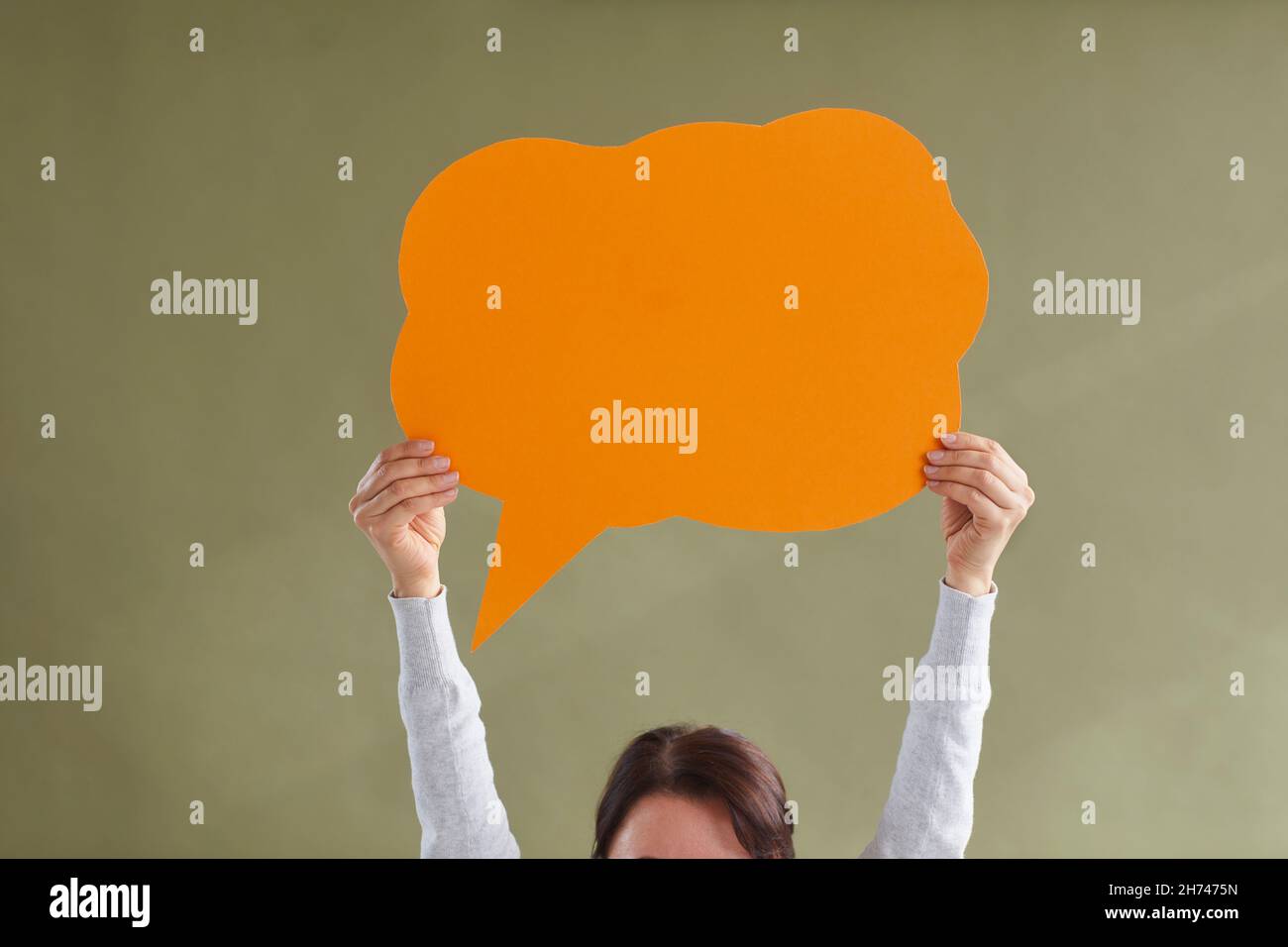 Woman holding one orange blank free speech bubble layout with place for text on green background. Stock Photo