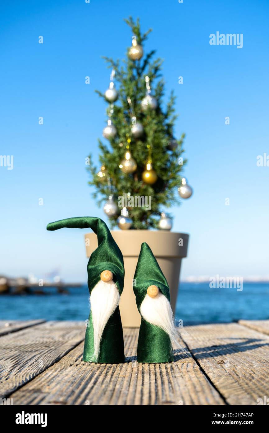Santa's little elves next to a decorated Christmas tree on the pier. Green gnomes on a sunny day at the sea. Vertical photo Stock Photo