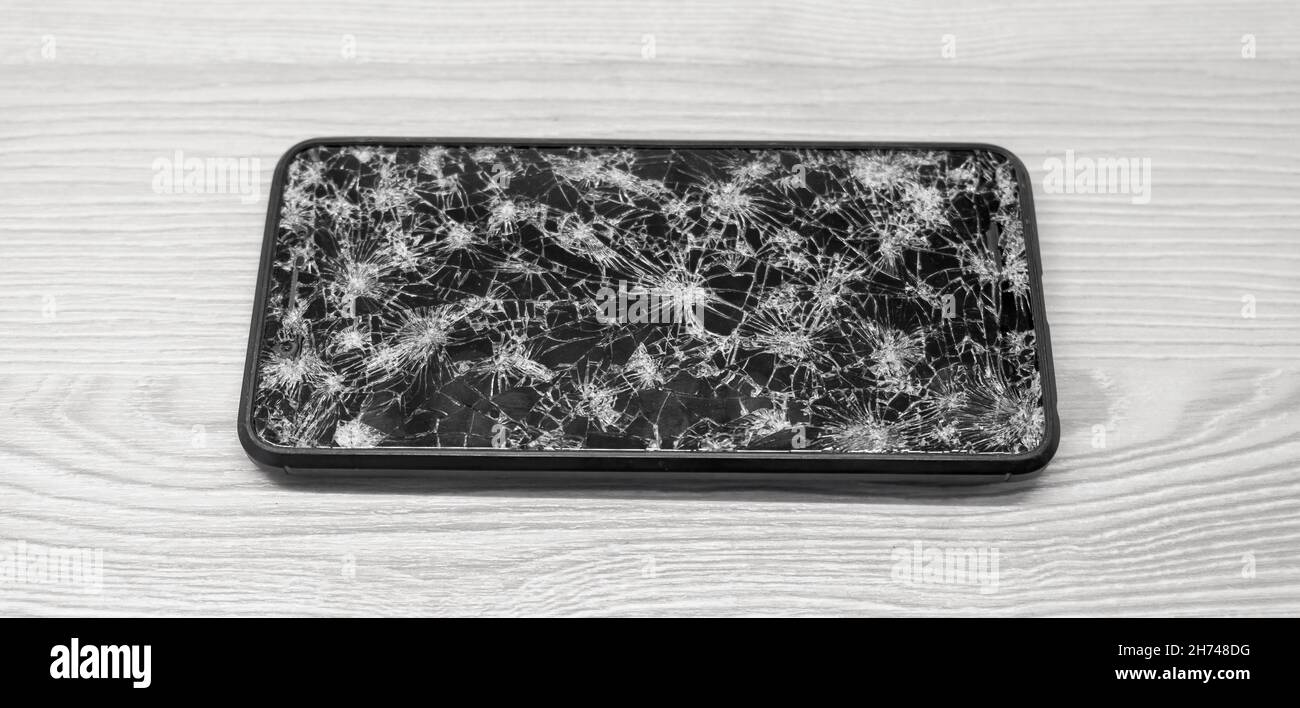 Modern touch screen smartphone with broken screen full of cracks on wooden background. Repair gadget concept Stock Photo