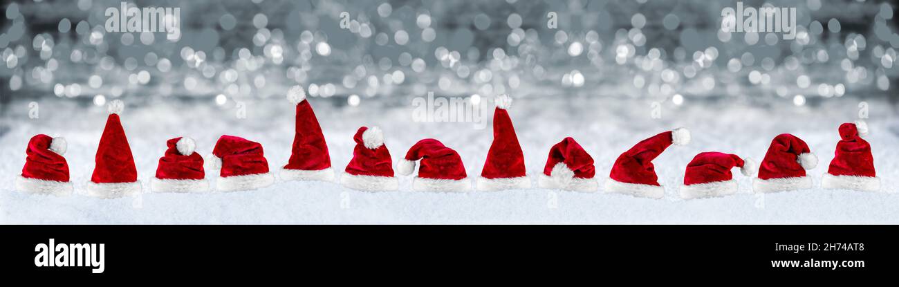 wide panorama row of red white plush santa claus christmas xmas hat on snow in front of silver gray bokeh lights background Stock Photo