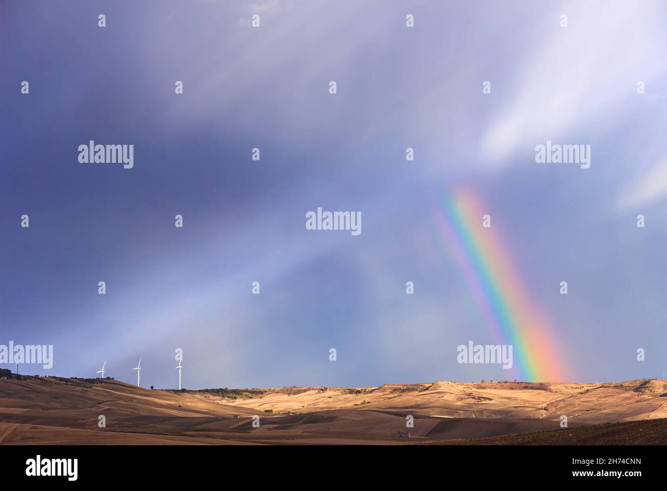 Renewable energy: wind power. Wind turbines in a dark sky with rainbow on a field in Apulia, Italy. Stock Photo