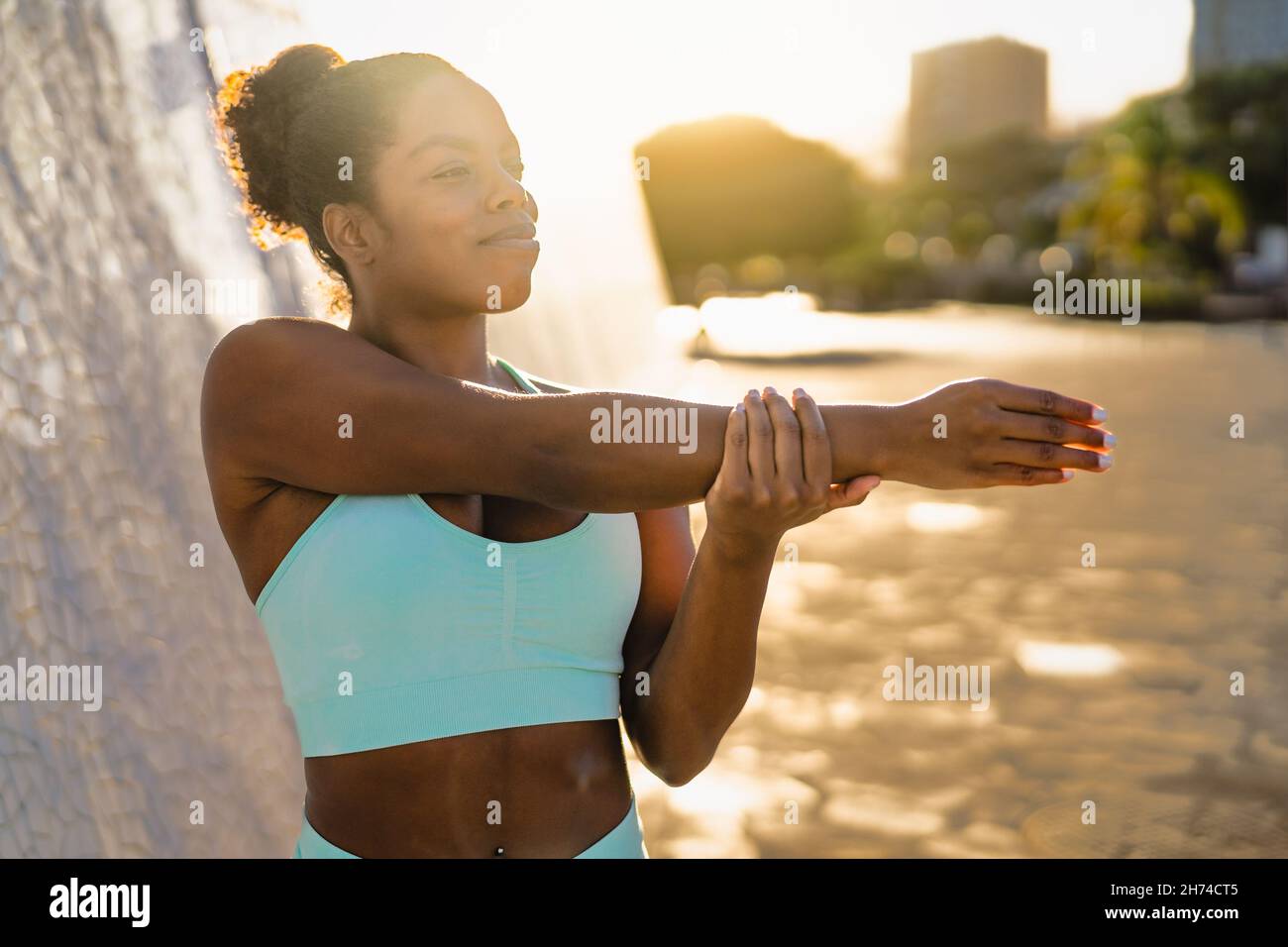 Young African woman doing warming up exercises before workout session in the city at sunset - Sport people lifestyle concept Stock Photo