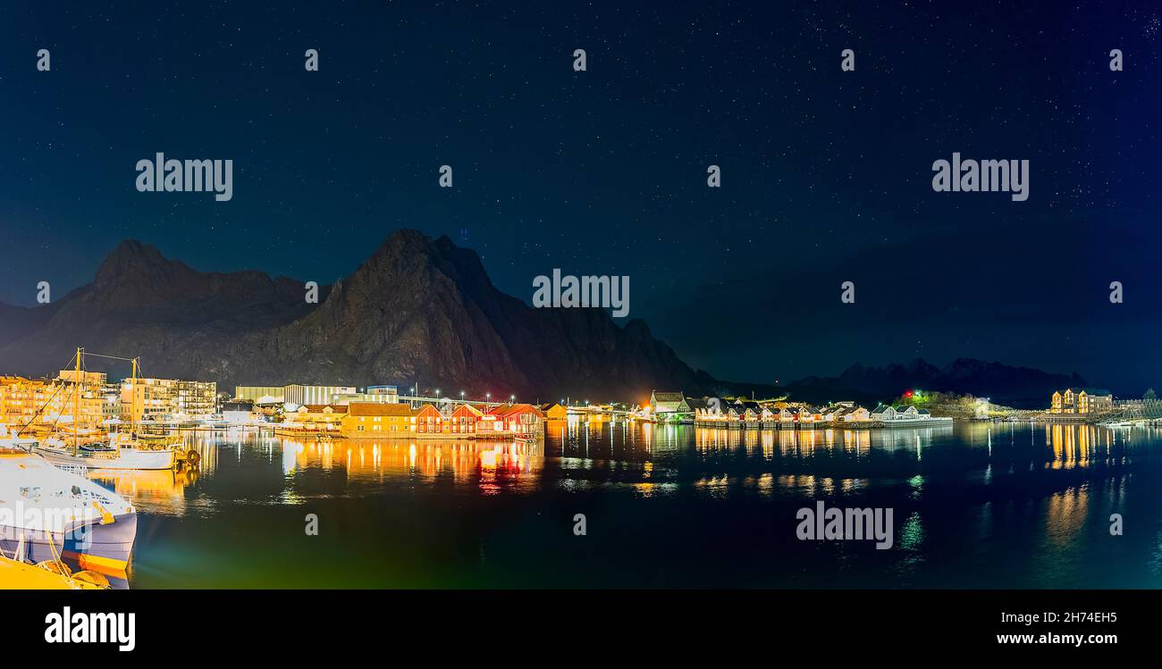 Svolvær auf den Lofoten, Norwegen, bei Nacht mit dem Djevelporten im Hintergrund. die beleuchtete Stadt spiegelt sich im Hafenbecken mit Schiffen Stock Photo