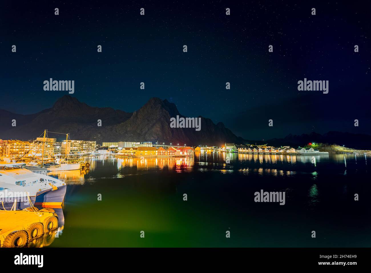 Svolvær auf den Lofoten, Norwegen, bei Nacht mit dem Djevelporten im Hintergrund. die beleuchtete Stadt spiegelt sich im Hafenbecken mit Schiffen Stock Photo