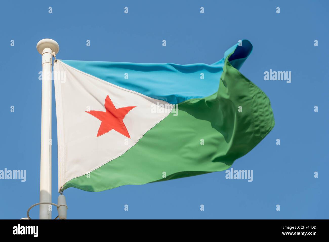 Djibouti Flag hanging and blowing in sunshine on blue sky background. Stock Photo