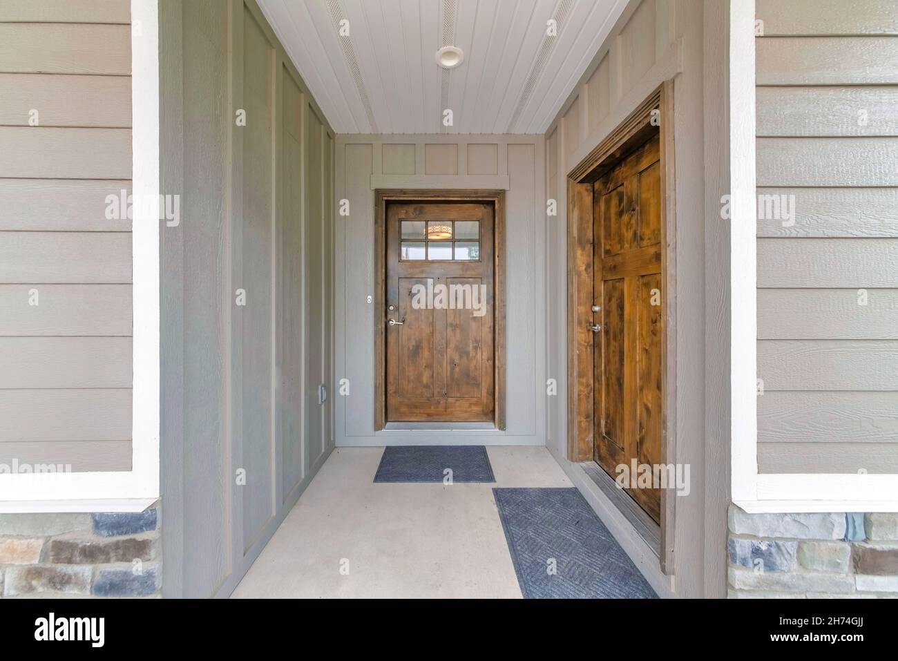 Two wooden front doors with glass panels and black doormats. House