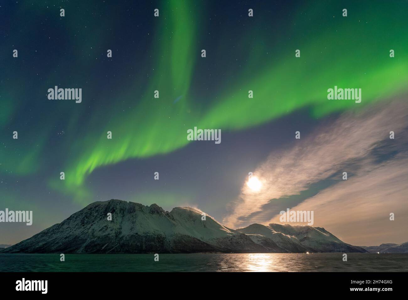 unterwegs in den Lyngenalps unter Nordlichtern. Vollmond mit Halo durch Eiskristallwolken. Aurora Borealis in Norwegen, vom Postschiff aus gesehen. Stock Photo