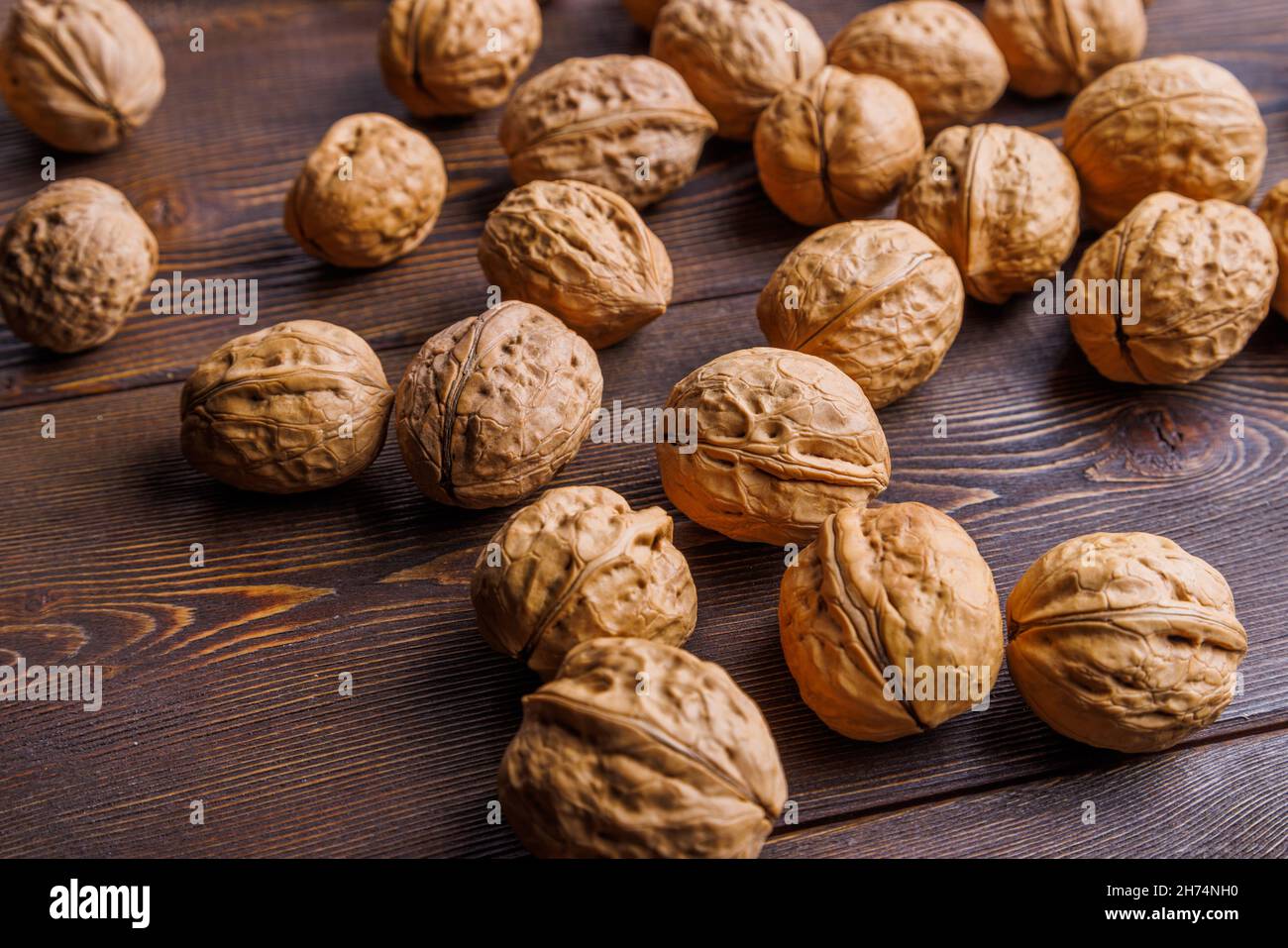 many walnuts with shells randomly scattered on brown wooden surface Stock Photo