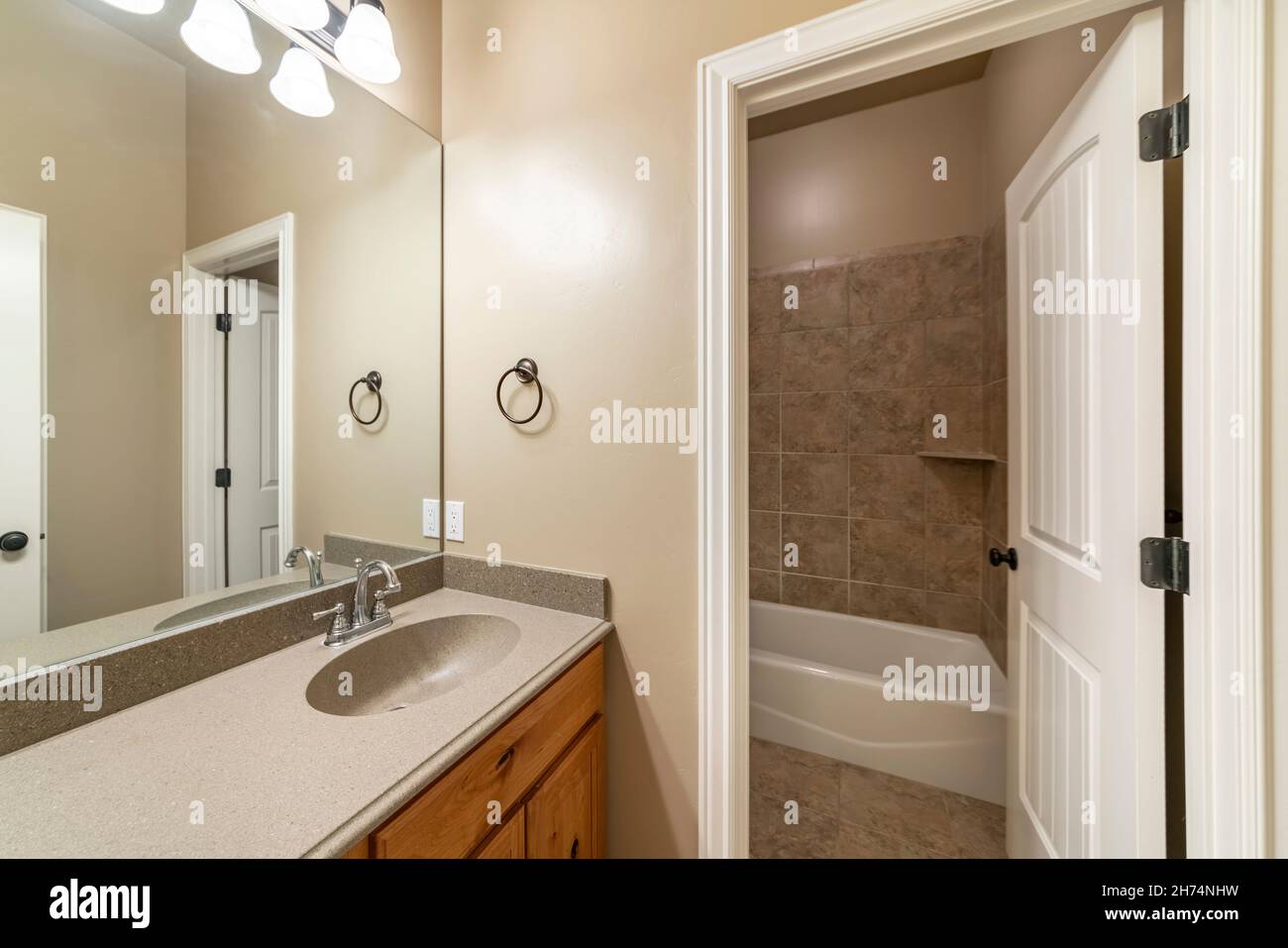 Bathroom interior with white doors and bathtub room with brown tiles corner  shelf and surround. There is a vanity sink with gray granite top and mirro  Stock Photo - Alamy