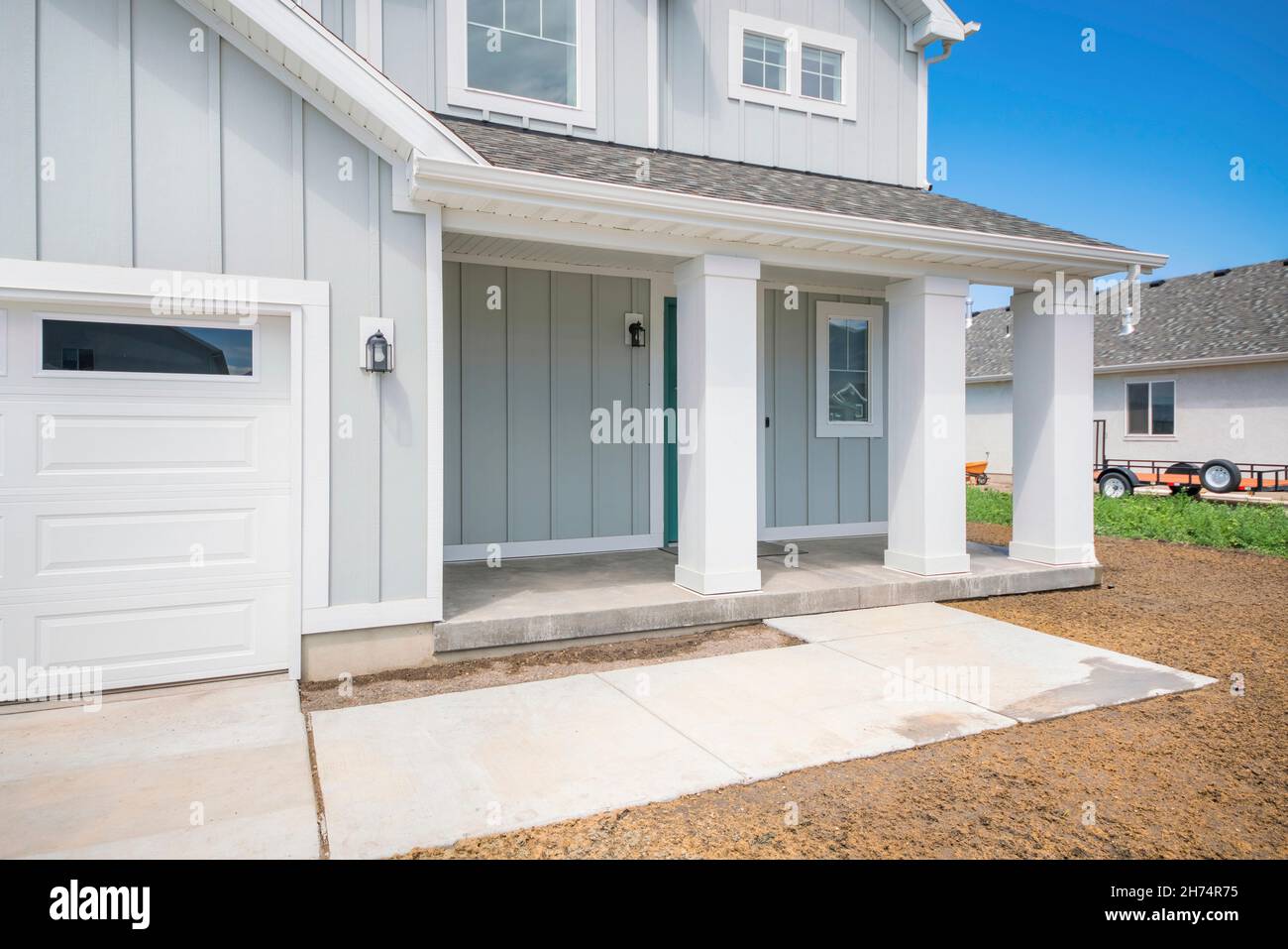 Exterior of a house with light gray board and batten siding and white column posts Stock Photo
