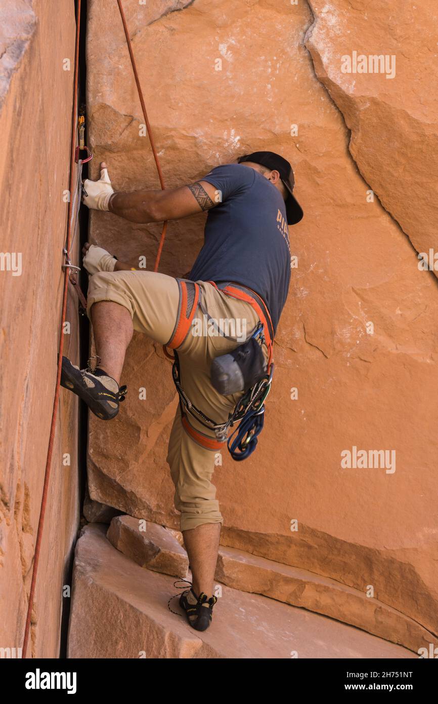 A climber arranges his hand holds on the difficult Bad Moki Roof route in the Wall Street climbing area, Moab, Utah. Stock Photo