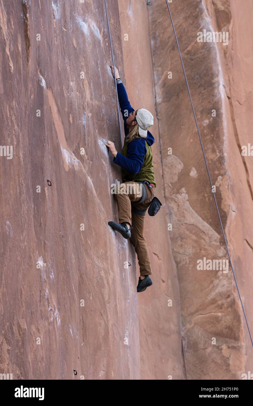 A climber reaches on the Nervous in Suburbia route in the Wall Street climbing area by Moab, Utah. Stock Photo