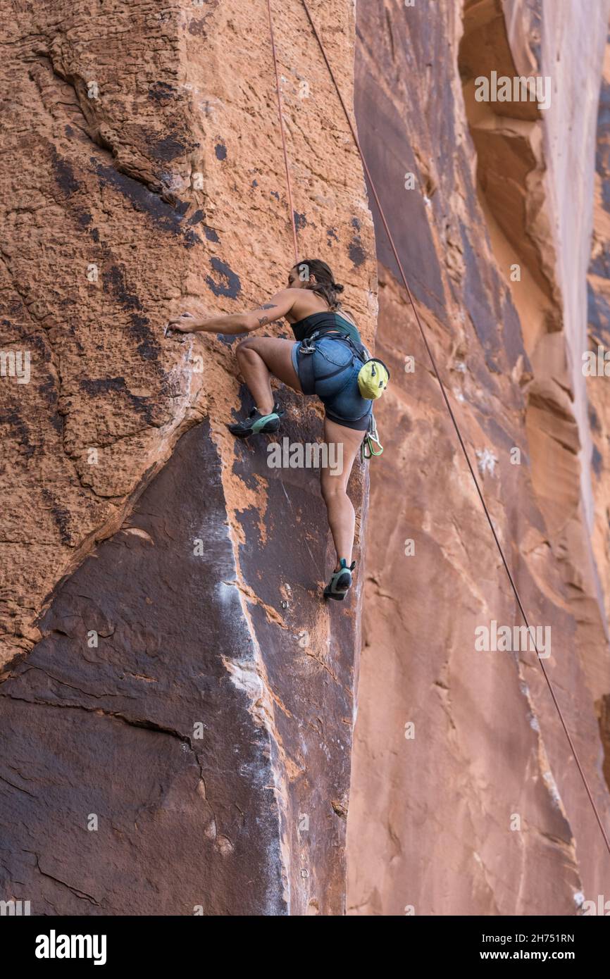 A woman rock climber on the very difficult Under the Boardwalk route on Wall Street, Moab, Utah. Stock Photo