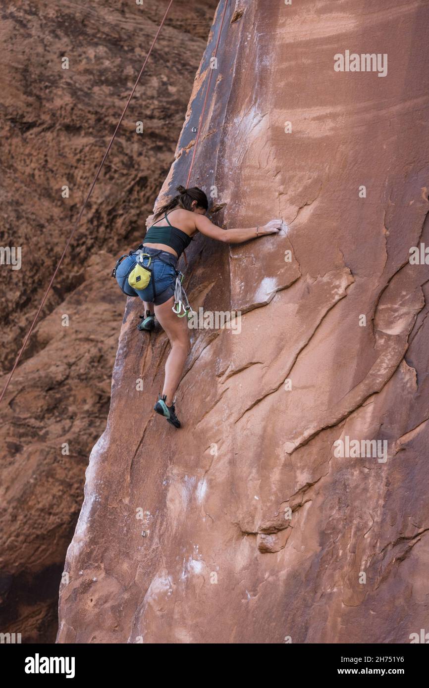 A woman rock climber on the very difficult Under the Boardwalk route on Wall Street, Moab, Utah. Stock Photo