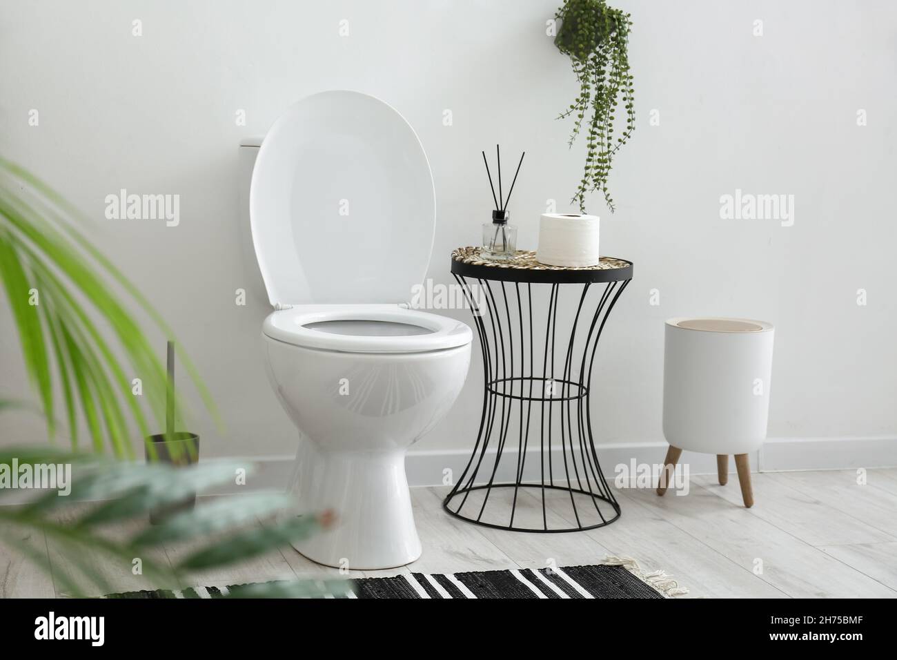 Toilet bowl, table with bathroom accessories and bin near white wall