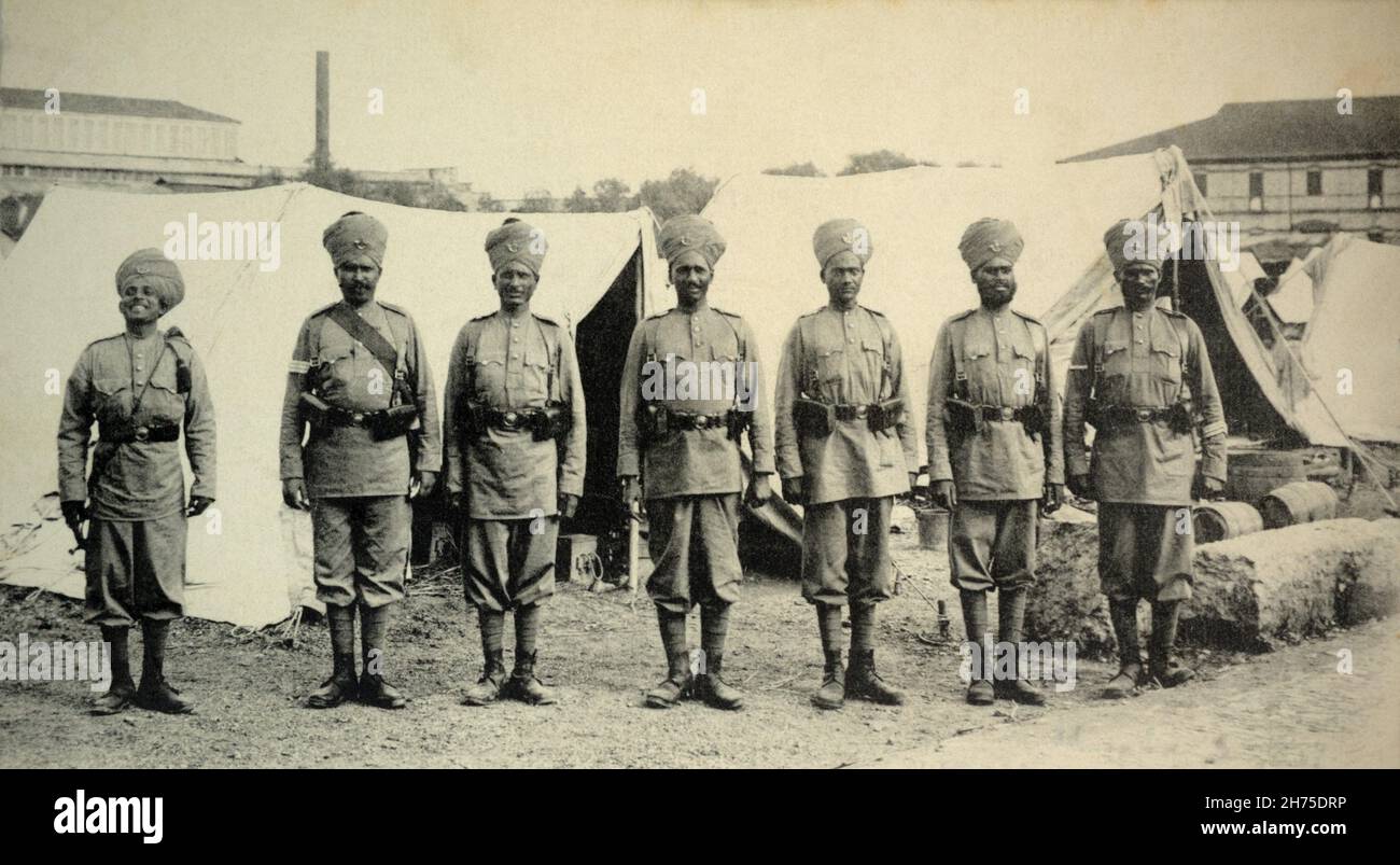A historical view of seven British Colonial Indian infantry soldiers, standing at attention in a camp, c. 1902. Stock Photo