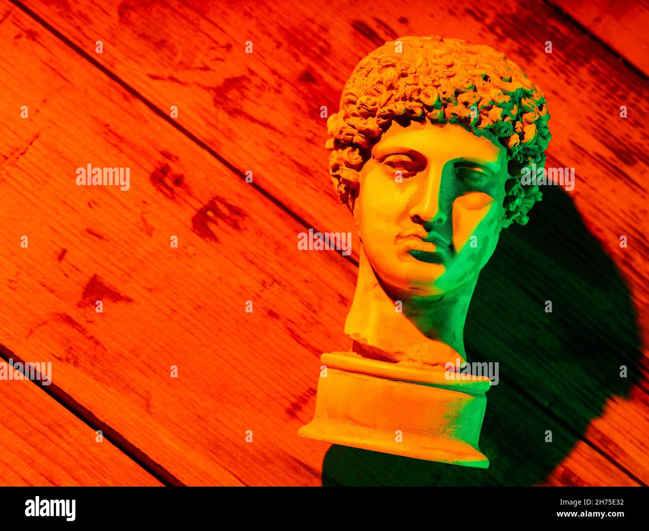 Gypsum copy of ancient statue Hermes head in orange green neon light. Neon image with ancient greek sculpture Hermes head. Minimal art fantasy concept Stock Photo