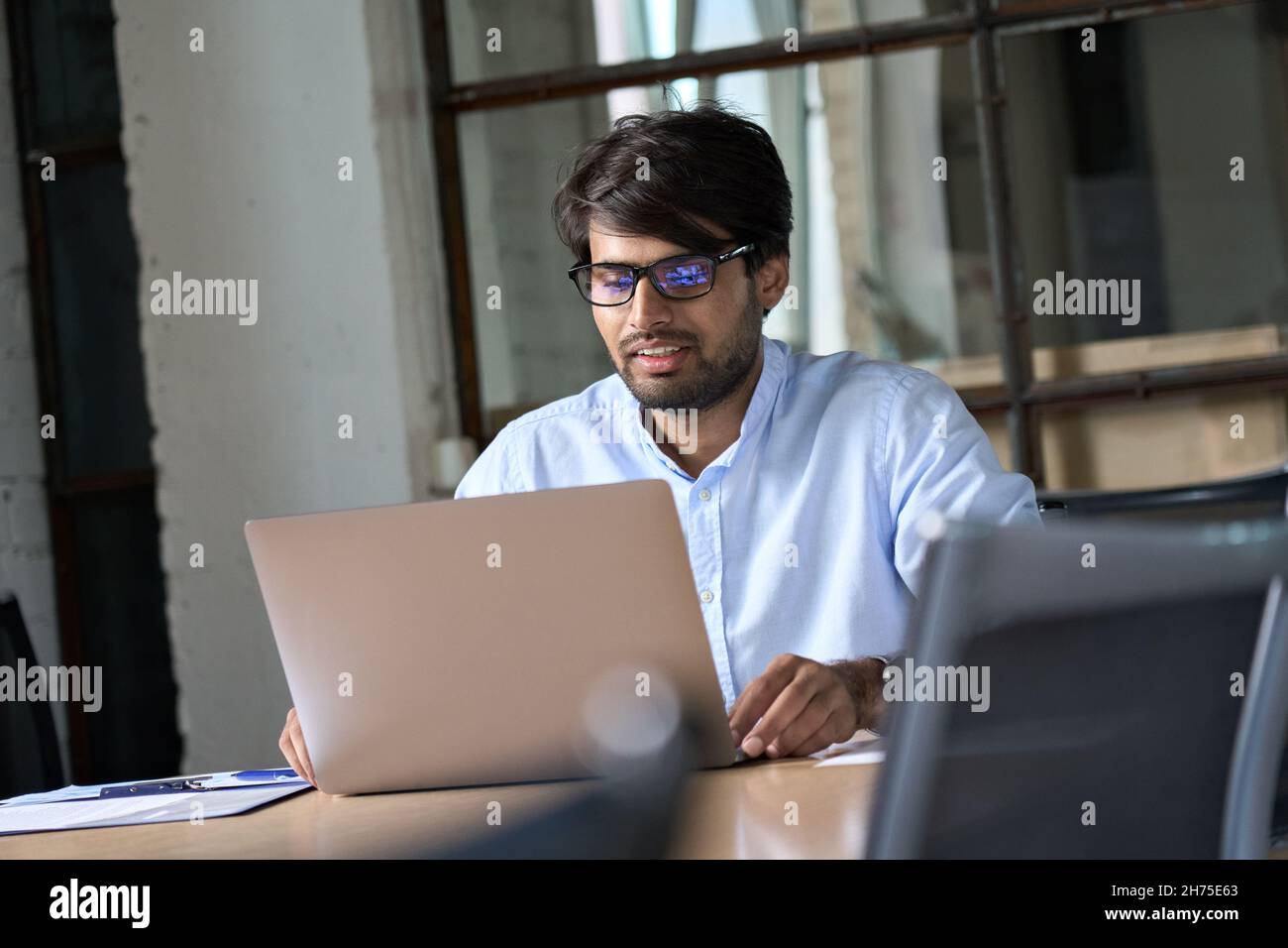 Young Indian businessman using laptop watching webinar in office. Stock Photo