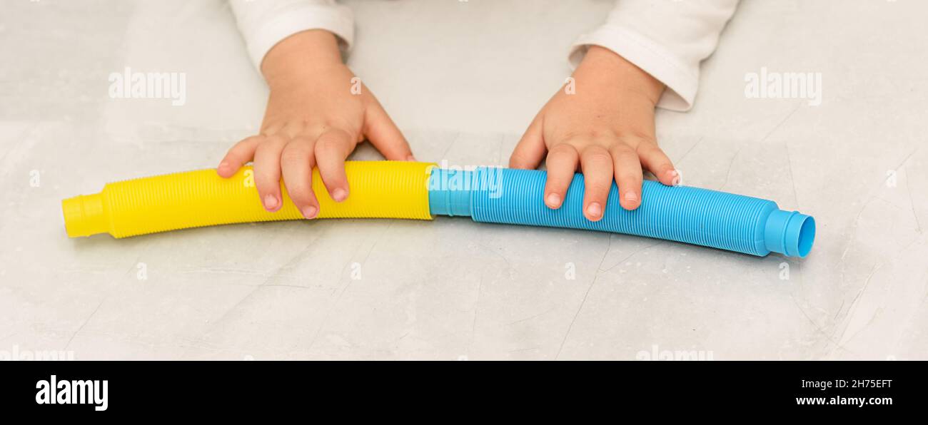 Anonymous child with colorful pop tube toy game. Close up banner shot of kid hands playing with pop tubes fidget toy. Stock Photo